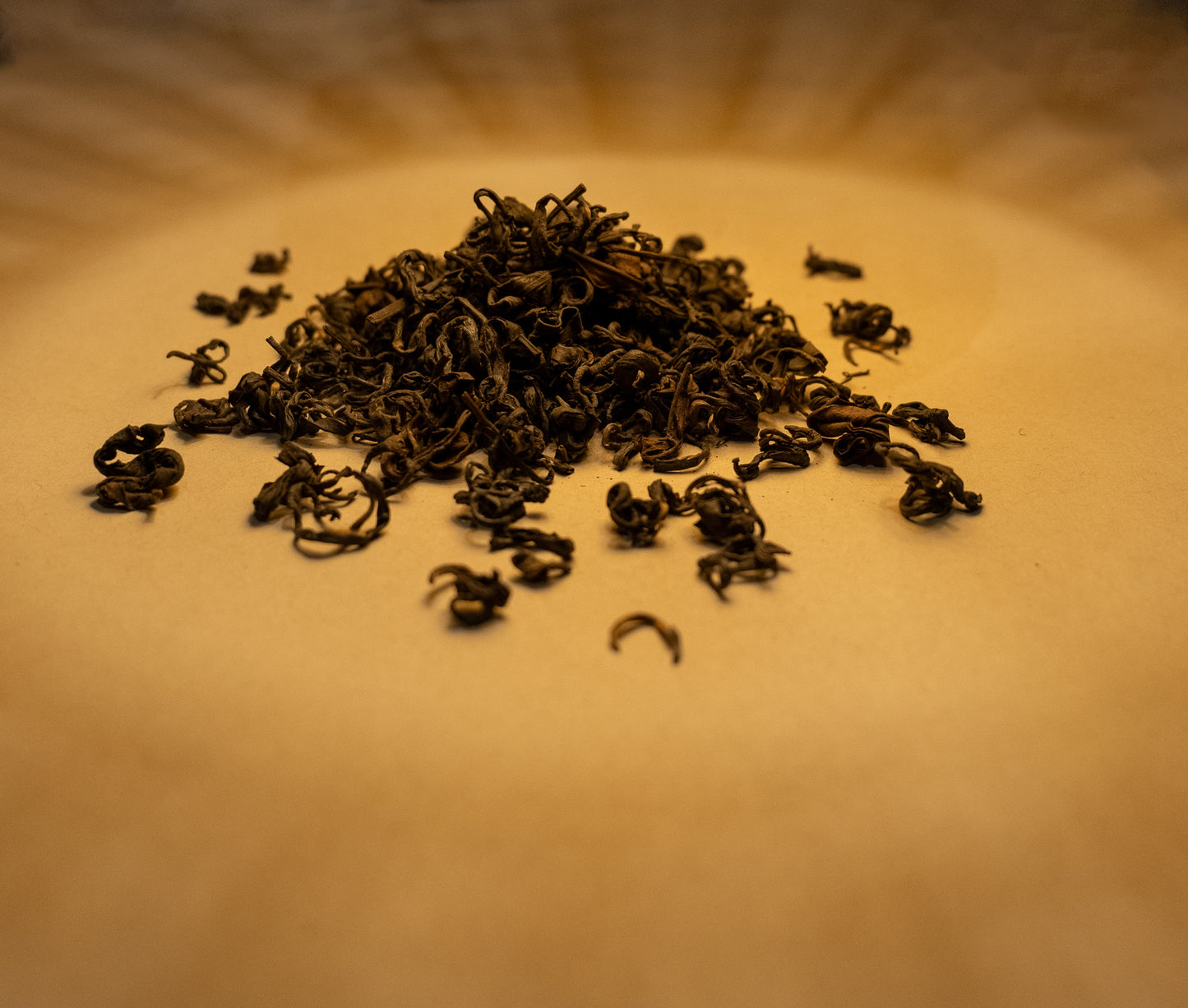 A pile of withered black tea leaves on an orange-brown surface. The warm colors and lighting suggest a natural and organic setting.