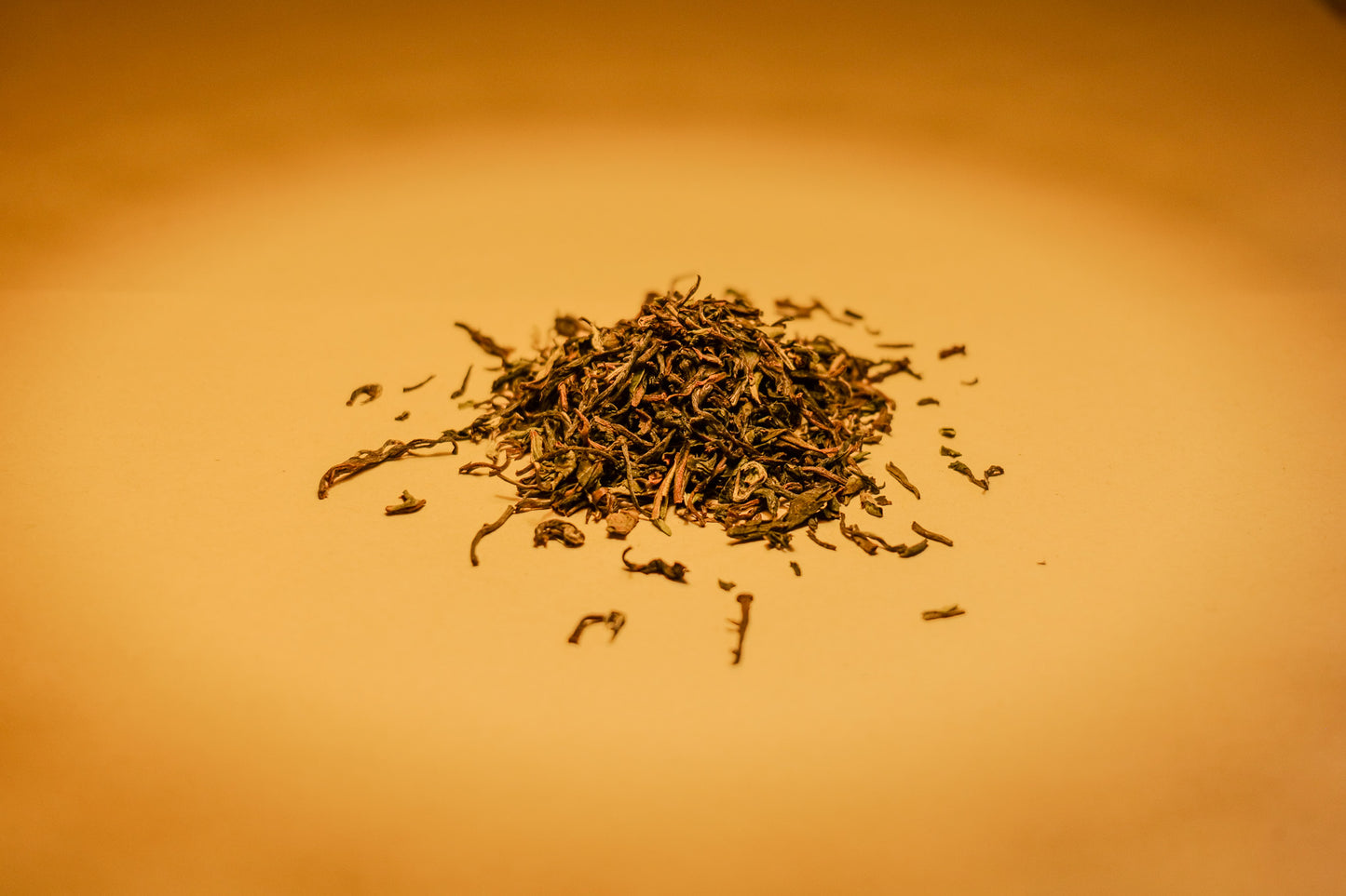 A pile of dried Darjeeling Orthodox black tea leaves on a warm orange-brown background.