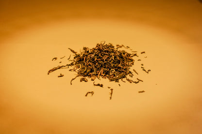 A pile of dried Darjeeling Orthodox black tea leaves on a warm orange-brown background.