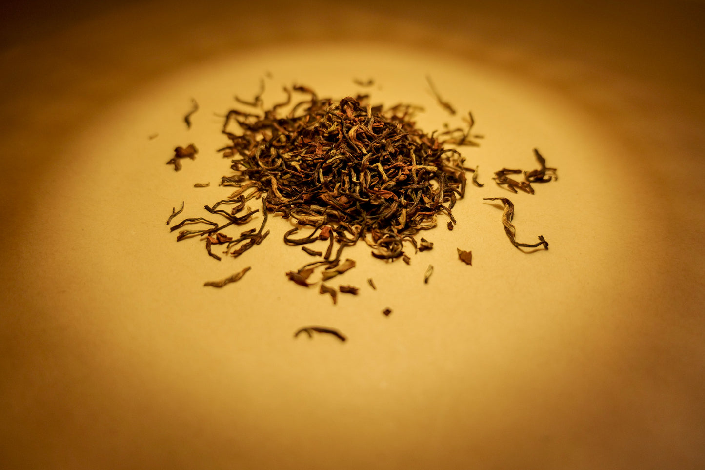 A pile of dried, twisted black tea leaves on a surface with a warm light overhead.