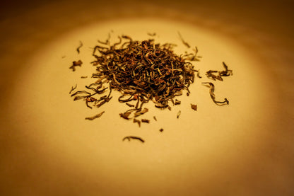 A pile of dried, twisted black tea leaves on a surface with a warm light overhead.