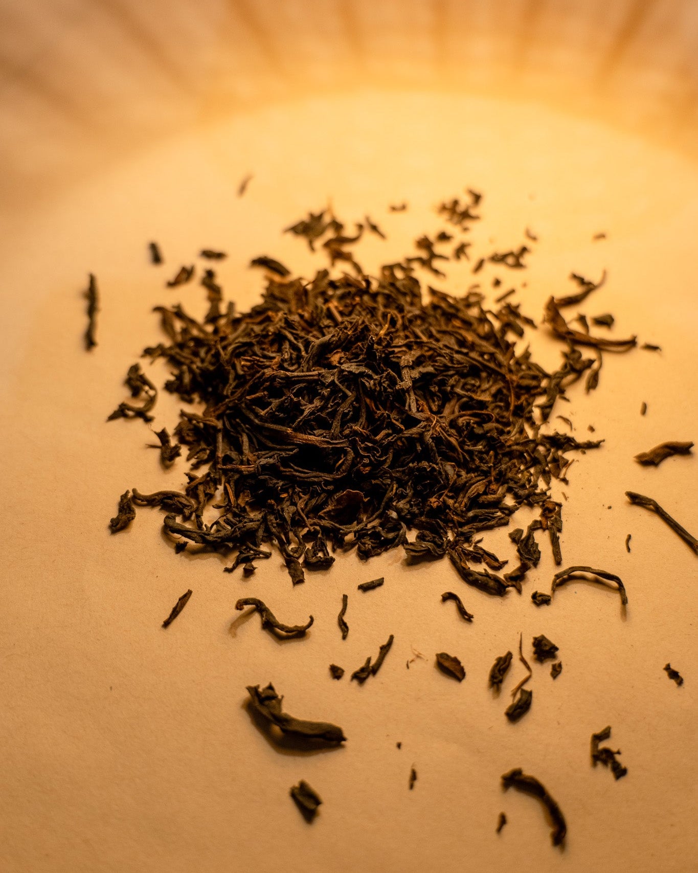 A pile of loose tea leaves on an orange-brown surface. The lighting and coloring is warm, suggesting a natural and organic setting.
