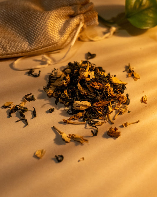 A scattered pile of dried jasmine green tea leaves and jasmine flowers on a light surface, with a burlap sack in the background.